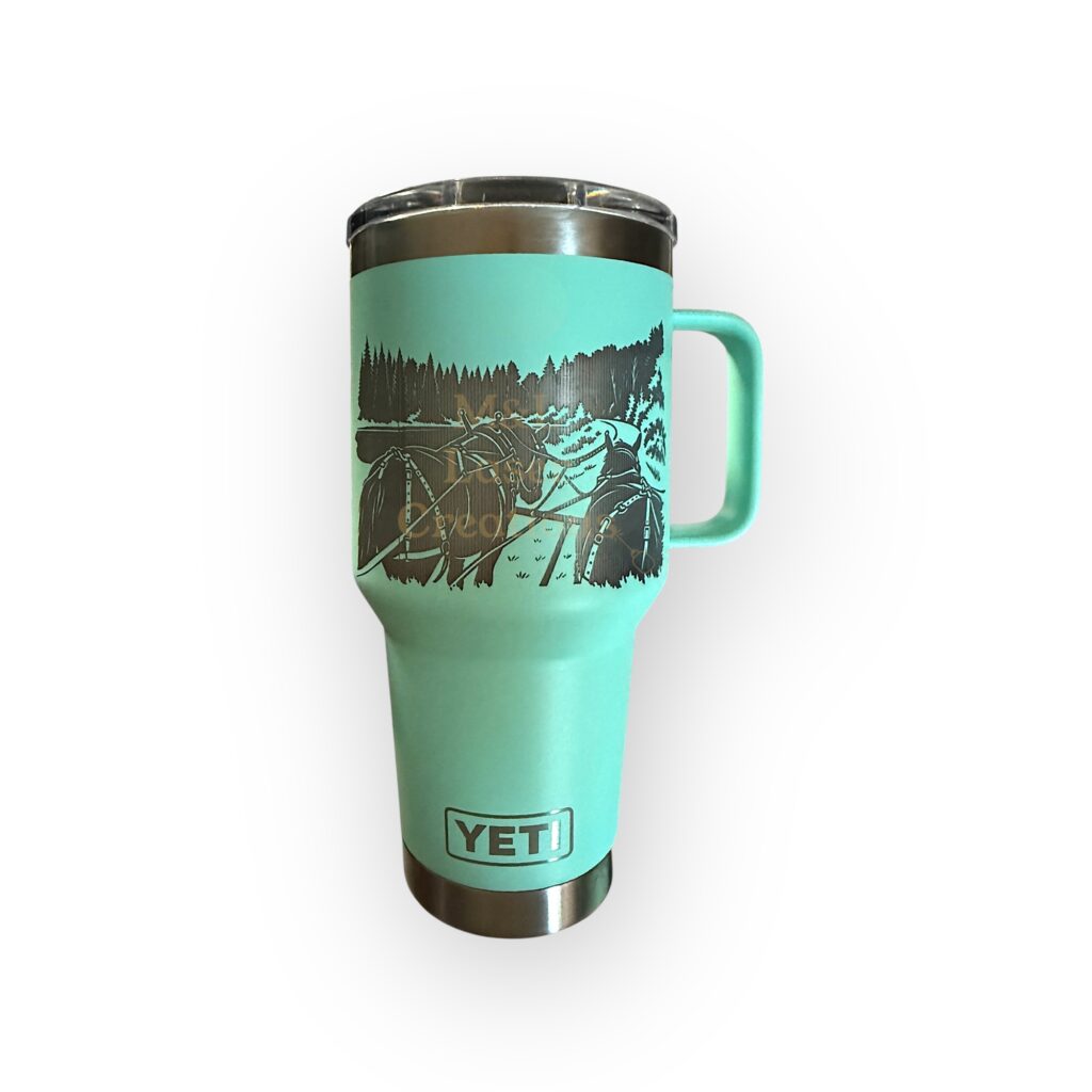 A seafoam yeti mug with handle laser engraved with a scene looking forward from a horse-drawn carriage.